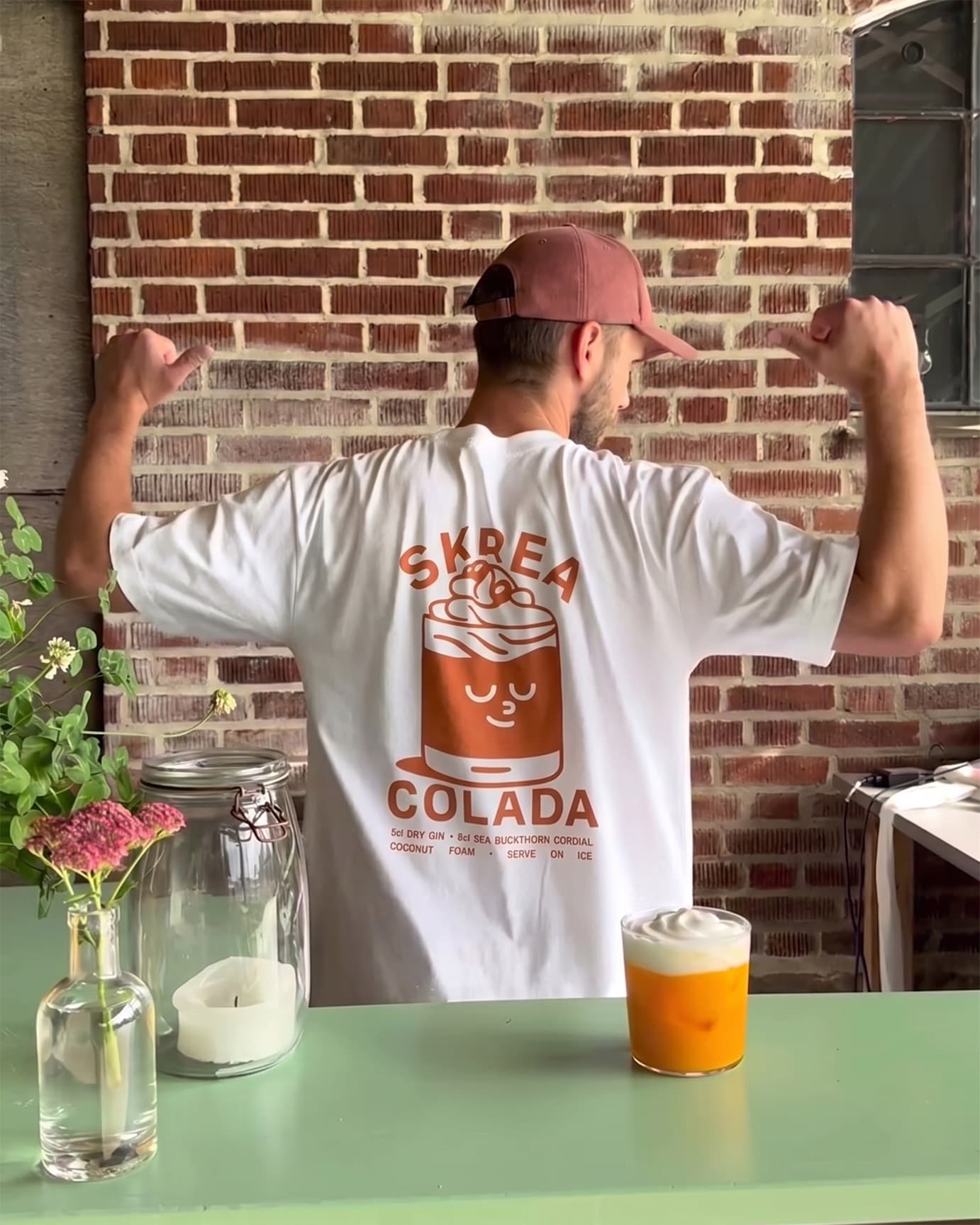 Man wearing the Skrea Backe tee outdoors at a table with a drink